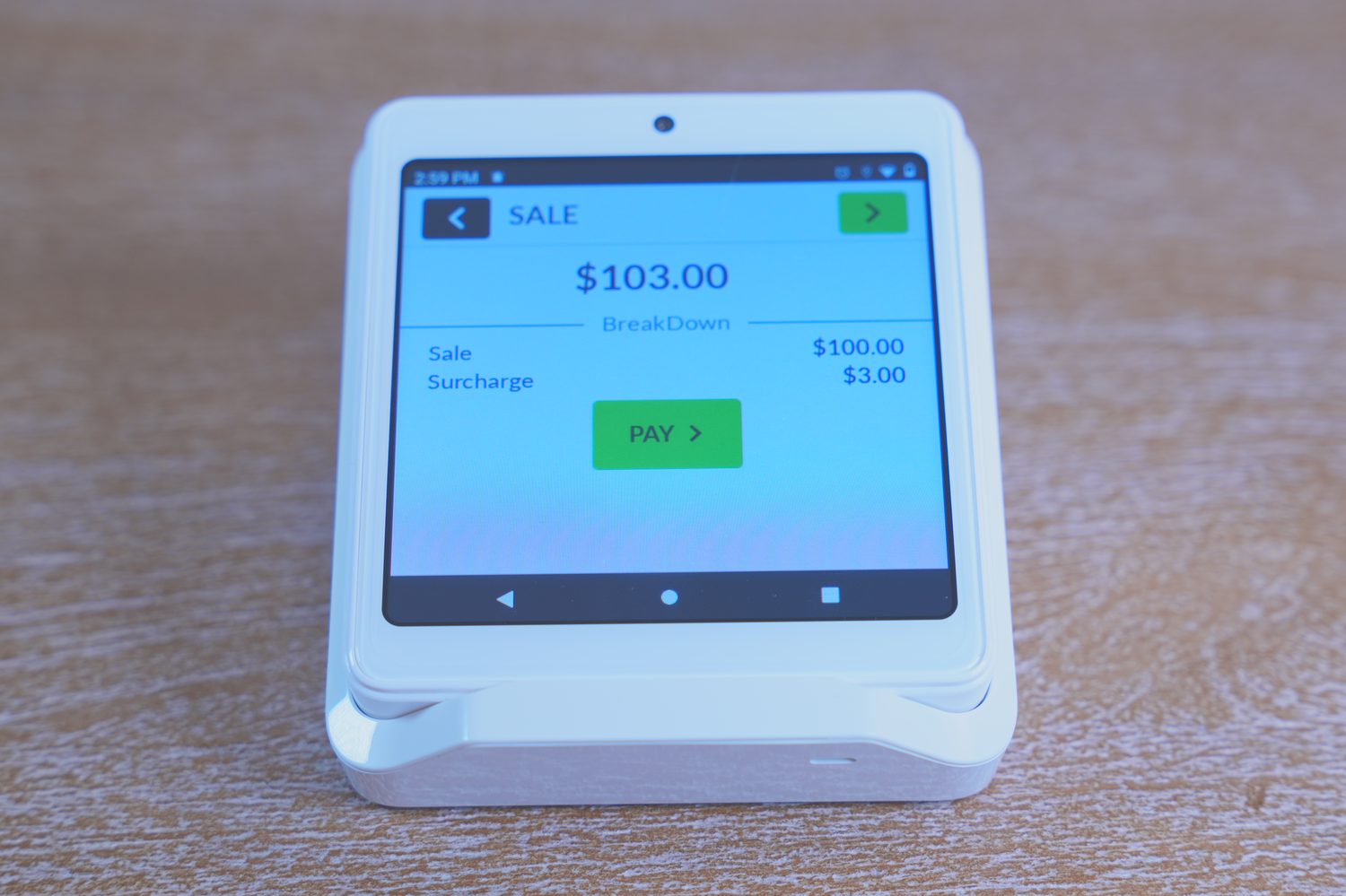 Payment terminal on a front desk showing a $103.00 sale broken down into a $100.00 sale and a $3.00 surcharge on its own line